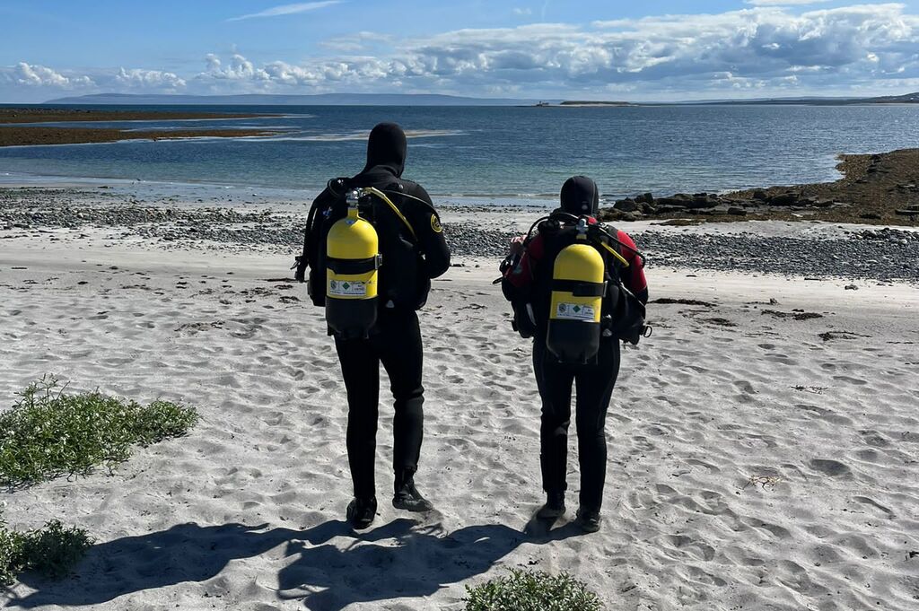 two scuba divers with dive gear walking on the beach for scuba diving in inishmore, aran islands