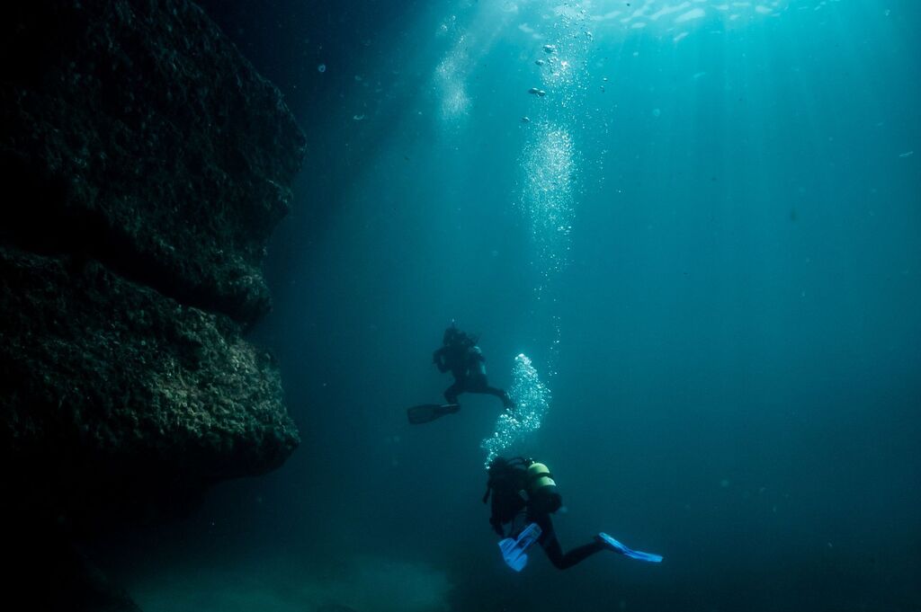scuba divers underwater exploring puffing holes one of most amazing dive sites in inishmore, aran islands